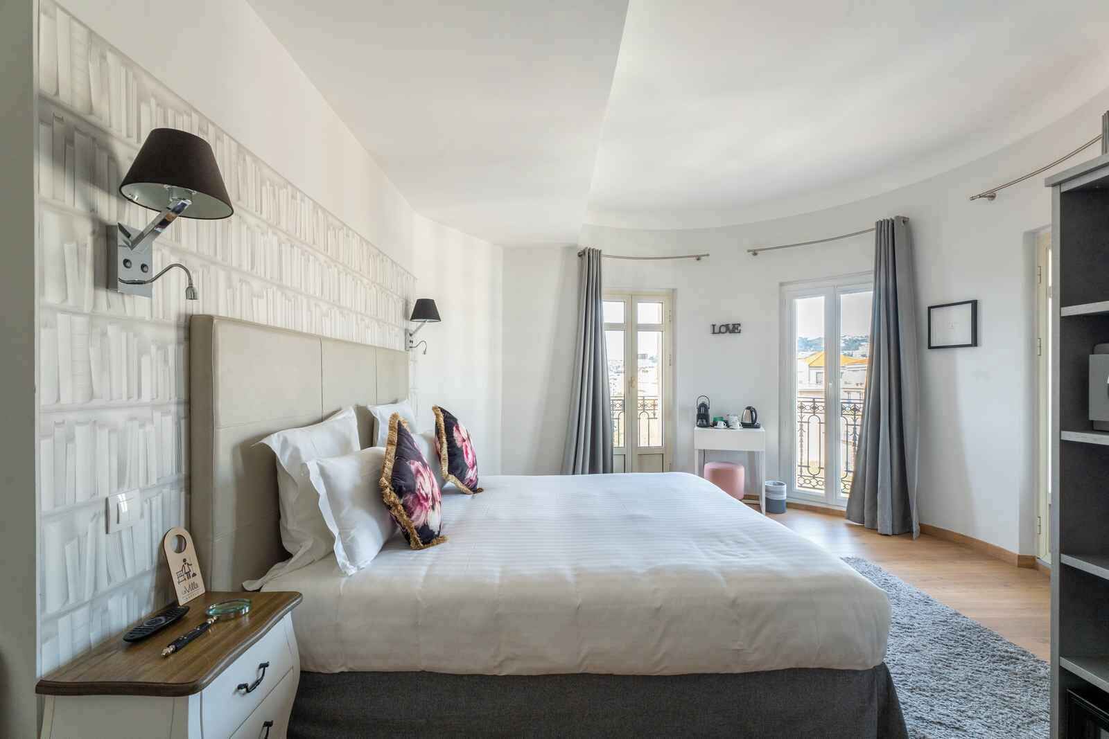 A bedroom with a bed, bedside tables, a desk, and a view through a window.