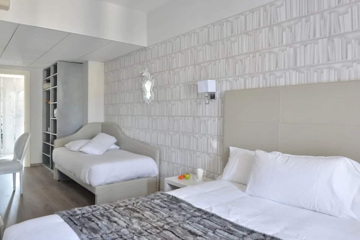 A hotel room with two beds, a wardrobe, a bedside table with a lamp, and a patterned wall.