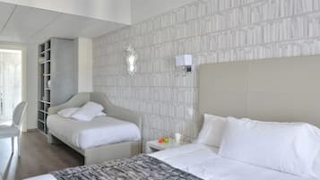 Habitación de hotel con dos camas, un armario, una mesita de noche con lámpara y una pared con estampado.