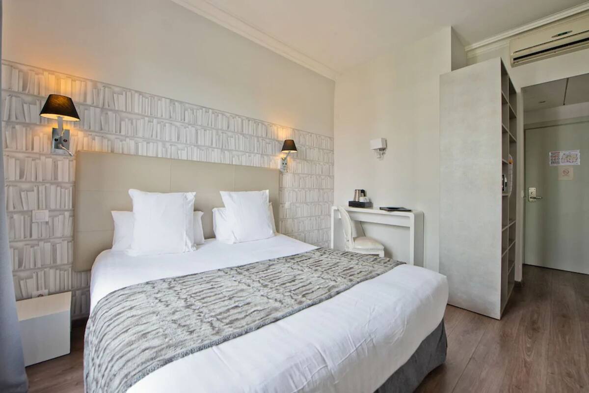 A hotel room with a large bed, a bedside table with a lamp, and a wardrobe.