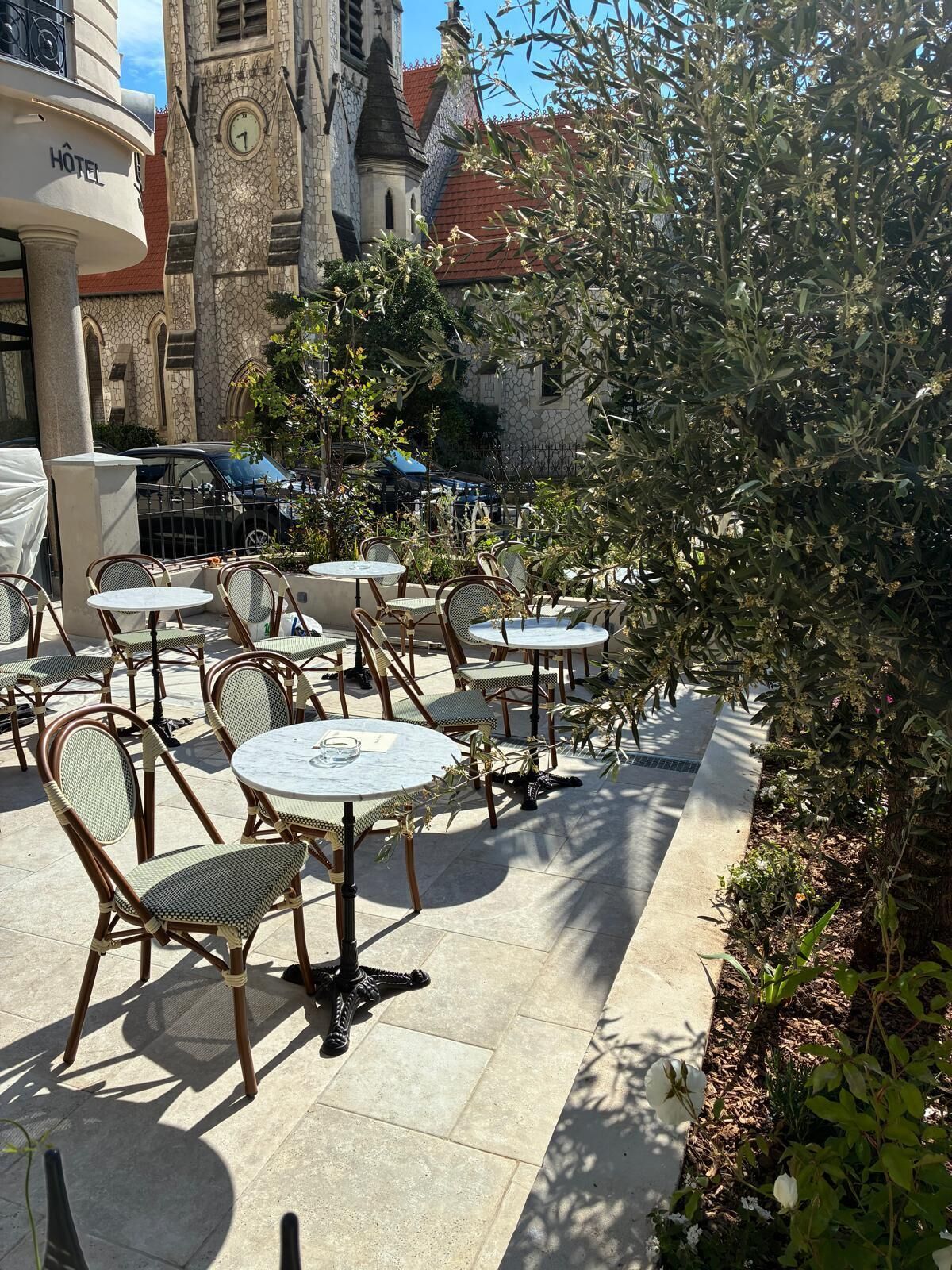 Outdoor patio seating with tables and chairs, a clock tower in the background, and a hotel sign.