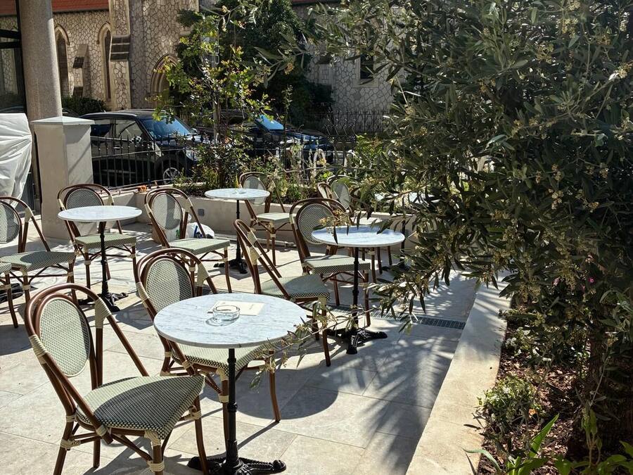 Outdoor patio seating with tables and chairs, a clock tower in the background, and a hotel sign.