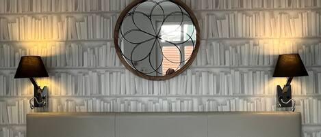 Una habitación de hotel con una cama grande, dos lámparas de noche, un panel decorativo en la pared y un espejo redondo sobre la cama.