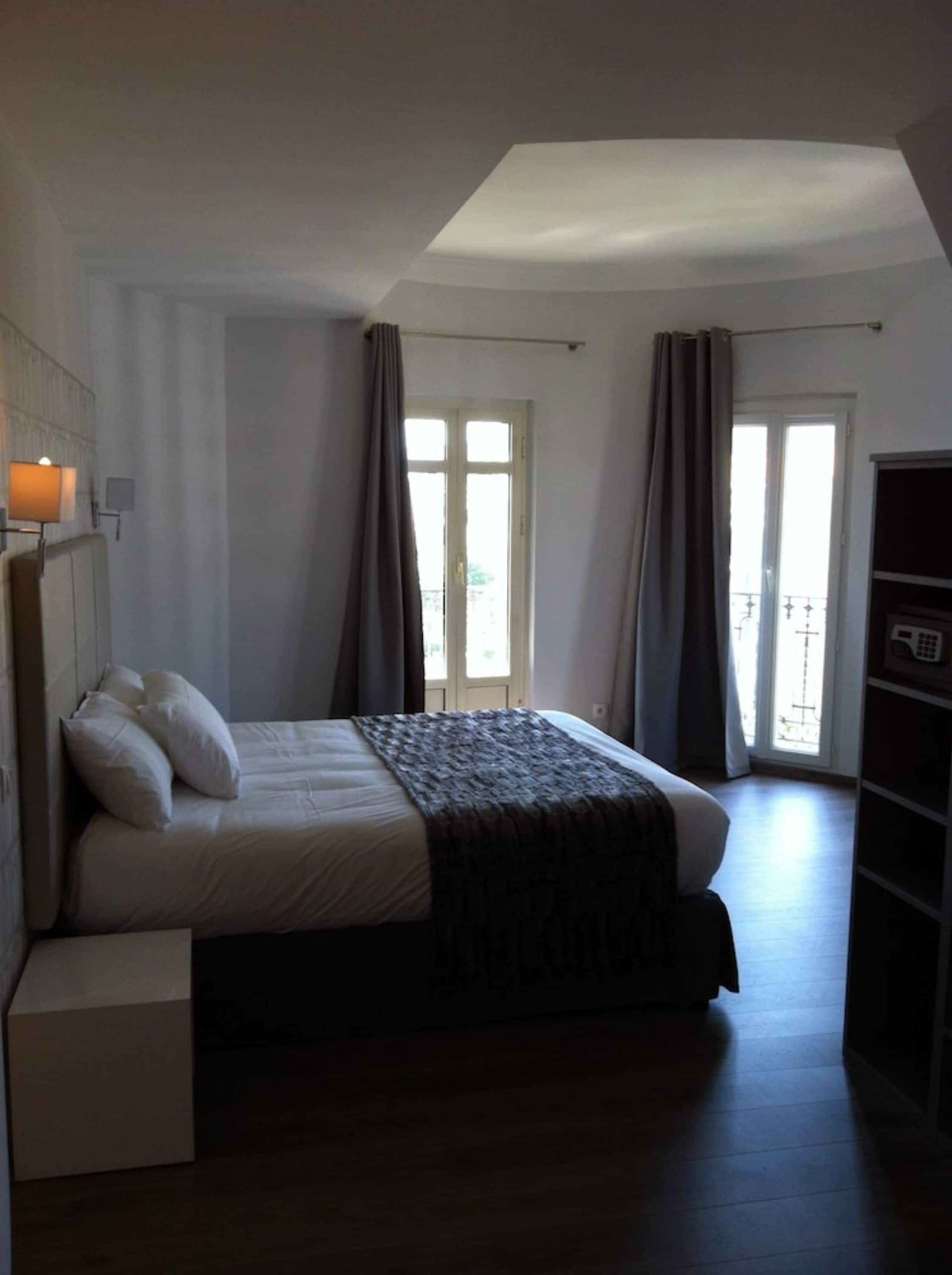 A bedroom with a bed, a bedside table, a wardrobe, and a window with curtains.