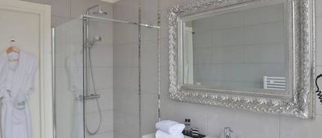 Un baño con cabina de ducha de vidrio, un lavabo blanco, un espejo grande y decorativo, y una bata blanca colgada en la pared.