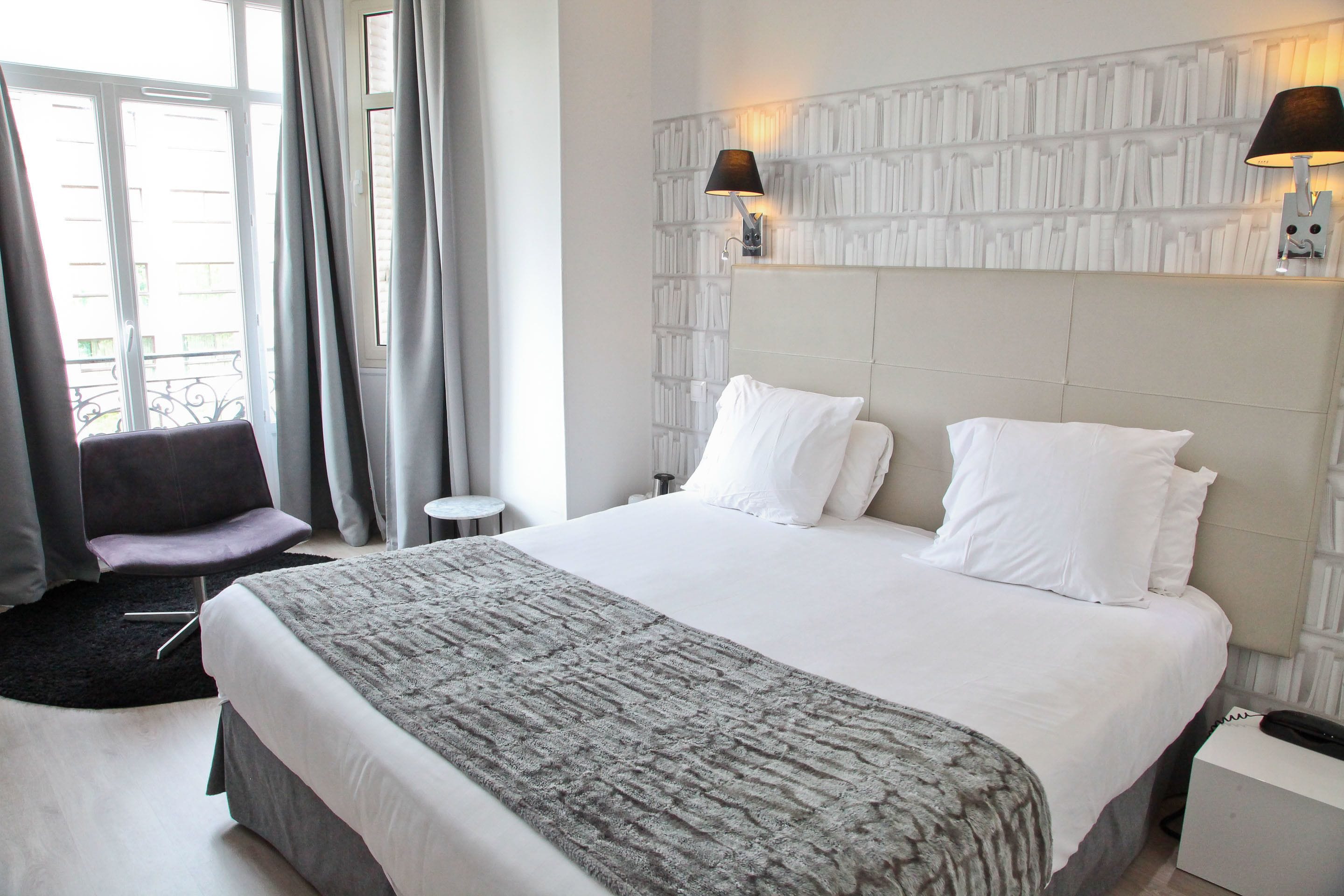 Une chambre d’hôtel avec un grand lit, une table de chevet, une chaise et une fenêtre avec des rideaux.