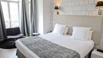 A hotel room with a large bed, a bedside table, a chair, and a window with curtains.
