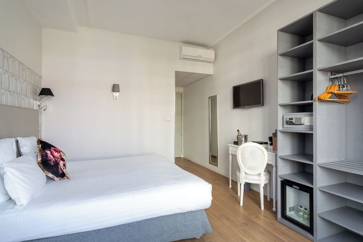 A bedroom with a bed, a desk, a chair, a TV, and a built-in wardrobe.