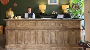 A reception desk with a wooden finish, three pendant lights, a framed portrait, and a potted plant. - Hôtel La Villa Nice Victor Hugo (Nice)