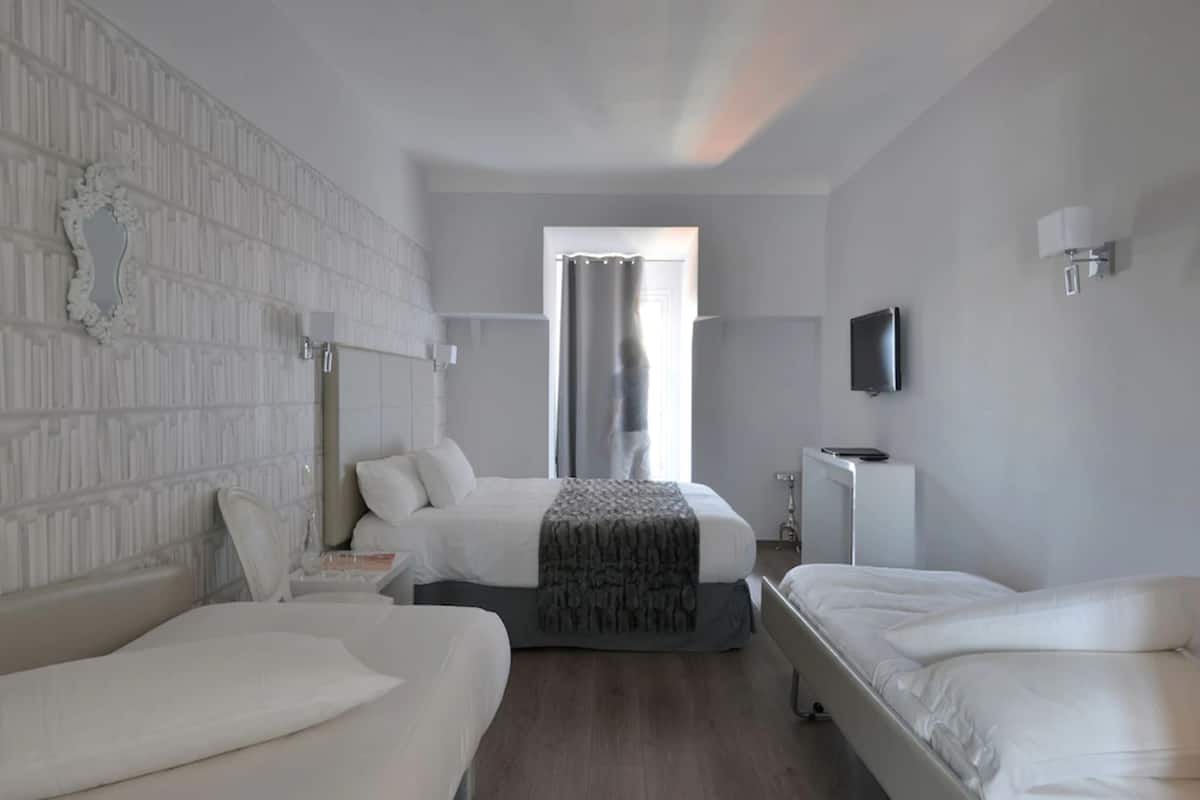 A hotel room with two beds, a television, a bedside table, and a window with curtains.