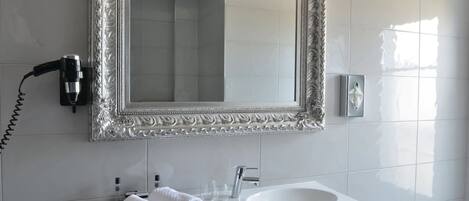 A bathroom with a white sink, a mirror with an ornate frame, a hairdryer, and a tissue dispenser.