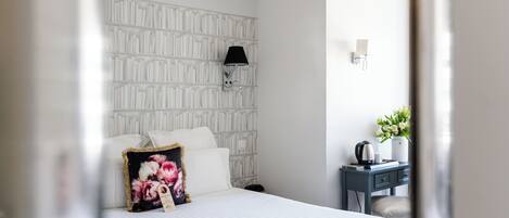 Une chambre d’hôtel avec un lit, une table de chevet, une lampe fixée au mur et une petite table sur laquelle est posé un vase de fleurs.