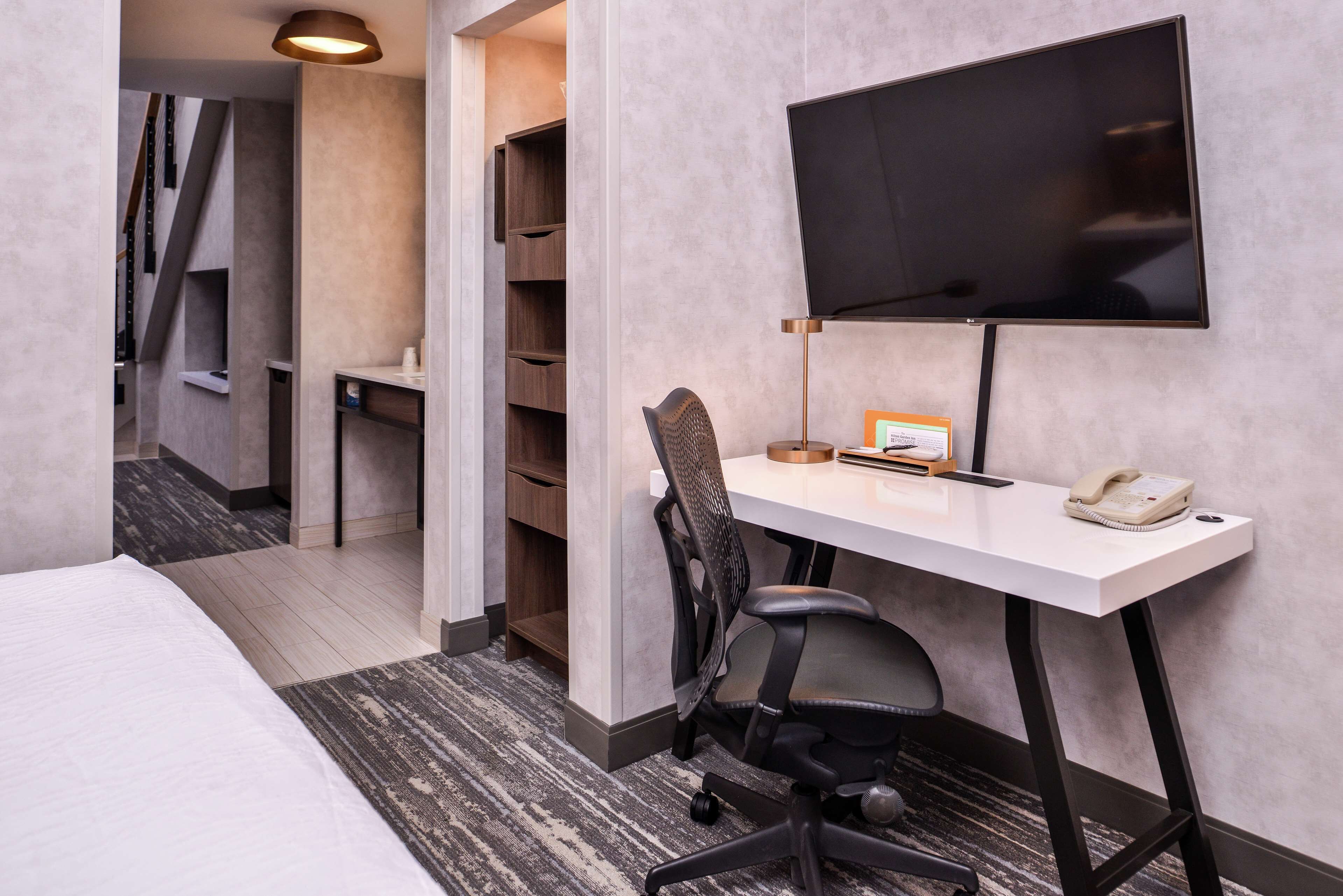 Habitación de hotel con cama, escritorio con silla, televisor de pantalla plana, teléfono y estantería.