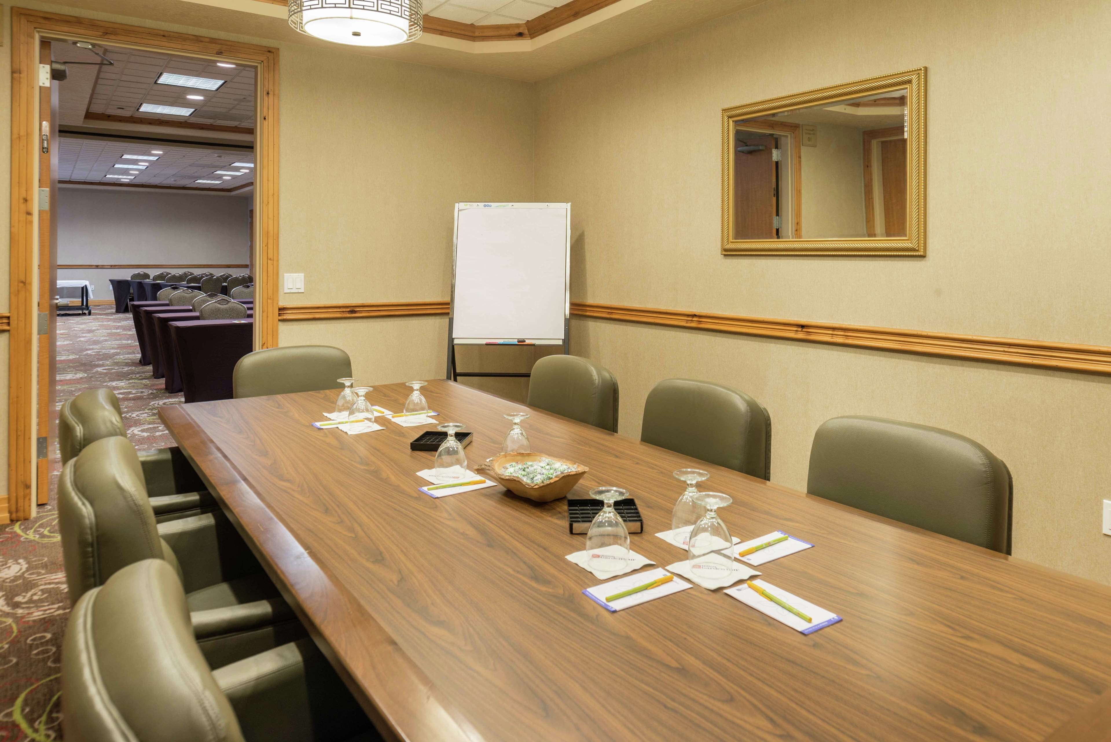 Un salón de conferencias con una larga mesa, sillas, una pizarra y un espejo en la pared.