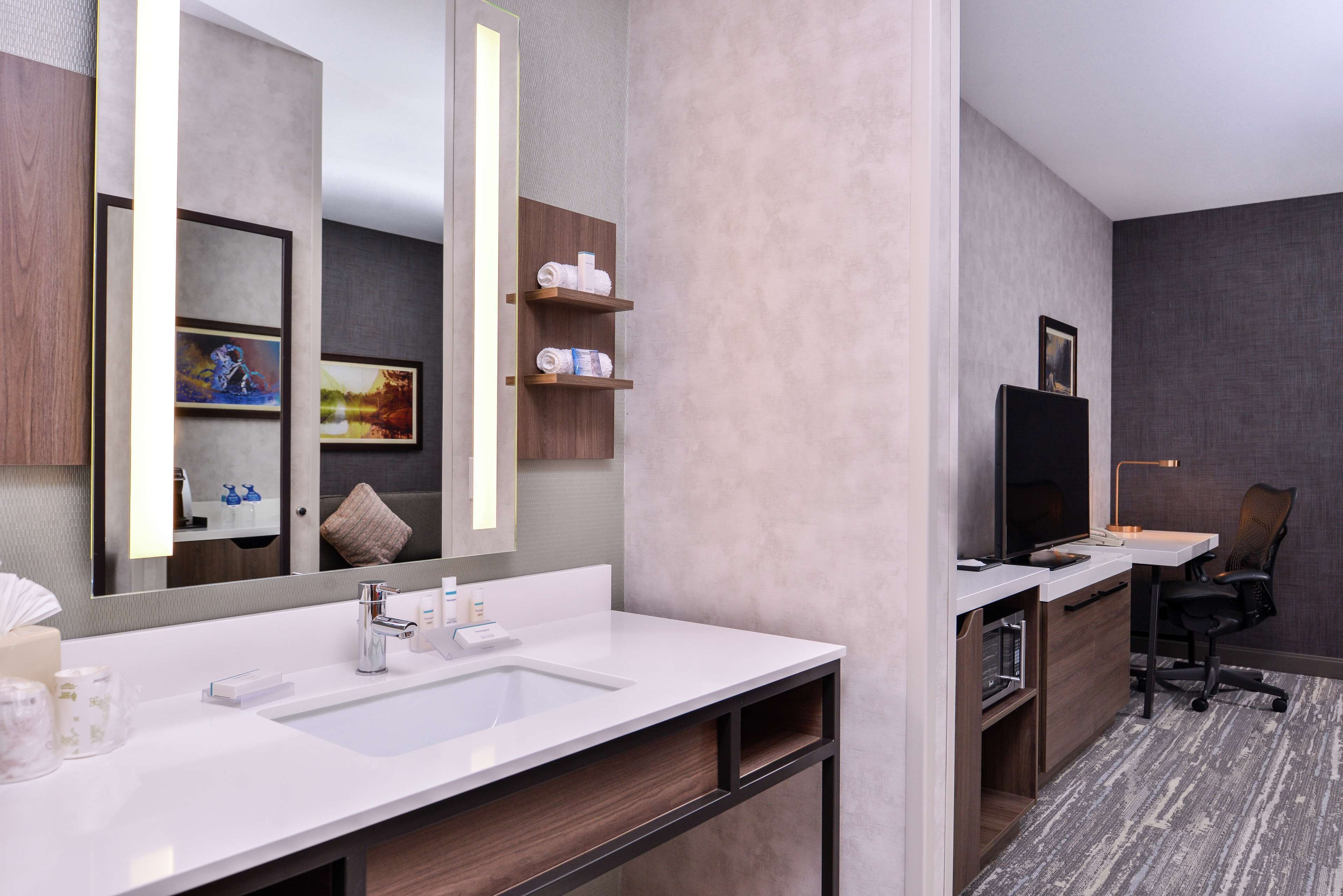 A modern bathroom with a large mirror, two sinks, a vanity, and a small desk with a chair.