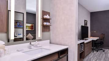 A modern bathroom with a large mirror, two sinks, a vanity, and a small desk with a chair.