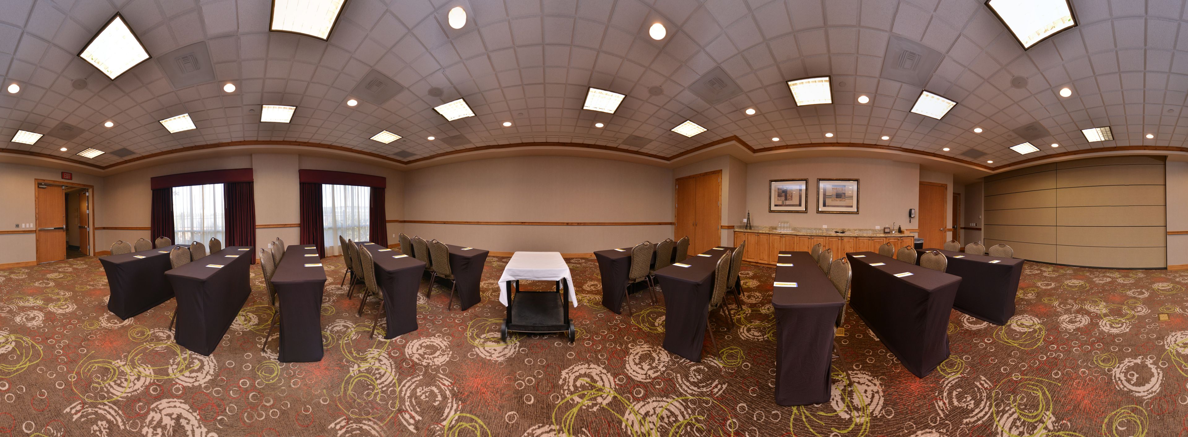A conference room with multiple tables and chairs, a carpeted floor, and a ceiling with recessed lighting.
