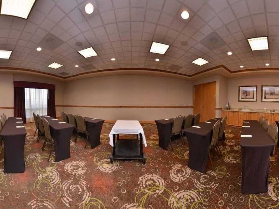 Une salle de conférence dotée de plusieurs tables et chaises, d’un sol recouvert de moquette et d’un plafond pourvu d’un éclairage encastré.