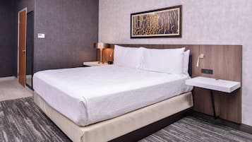 A modern hotel room with a large bed, bedside tables, a wall-mounted artwork, and a small bedside table.