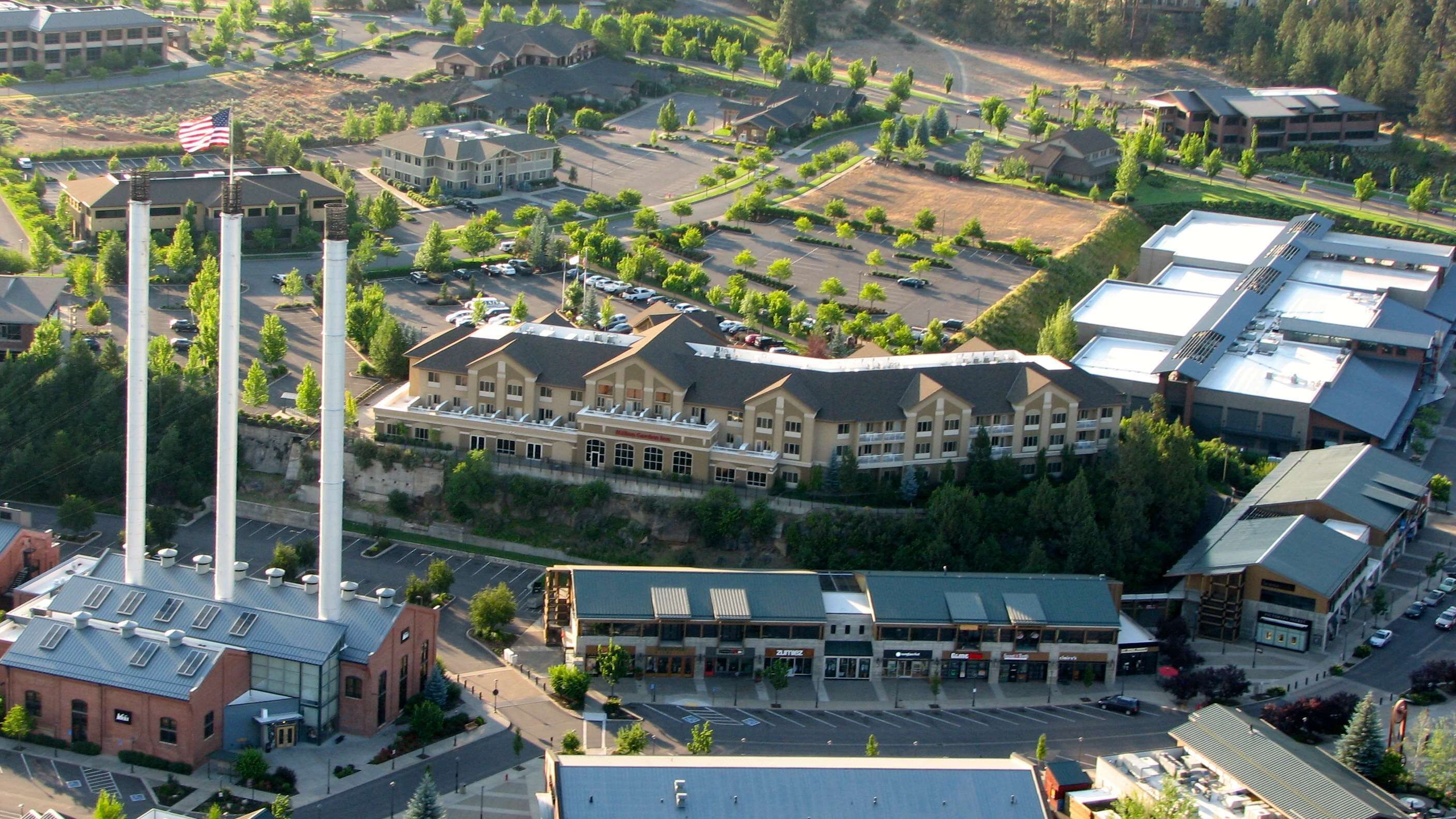 Ovenudblik over et hotel med en hovedbygning, parkeringsplads og grønne områder omkring.