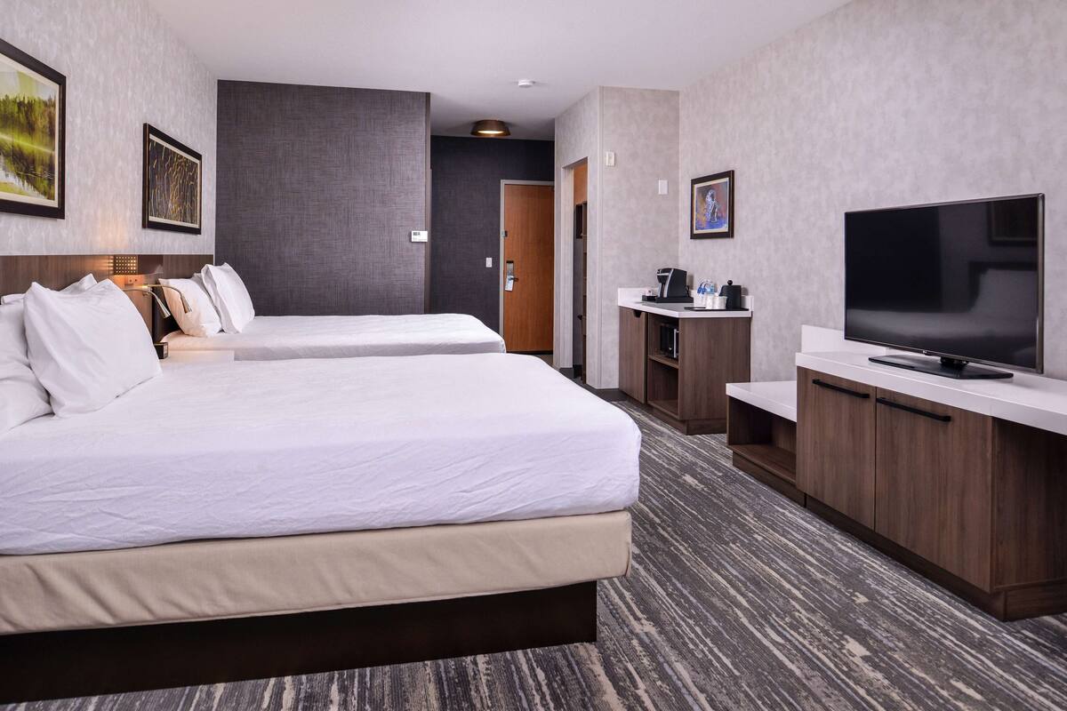 Quarto de hotel com duas camas, televisão, escrivaninha com cafeteira e obras de arte nas paredes.