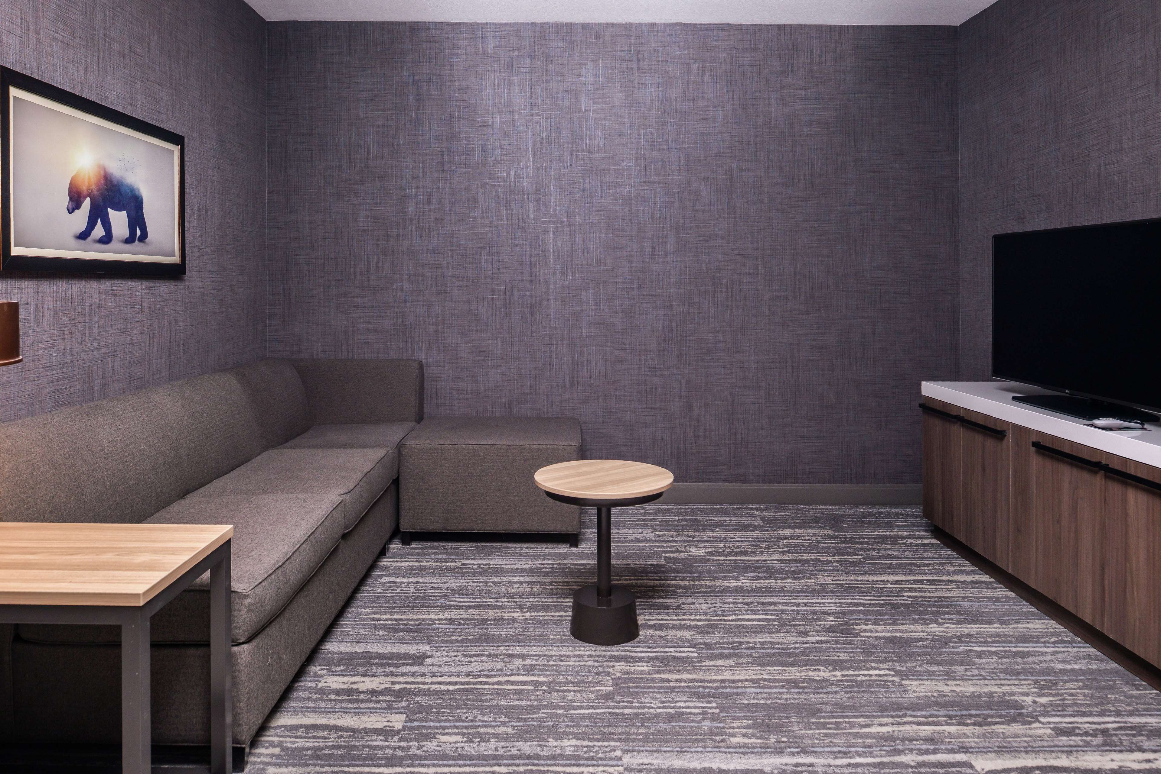Una sala de estar moderna con un sofá gris, una mesa de centro redonda de madera, un televisor de pantalla plana y un cuadro en la pared.