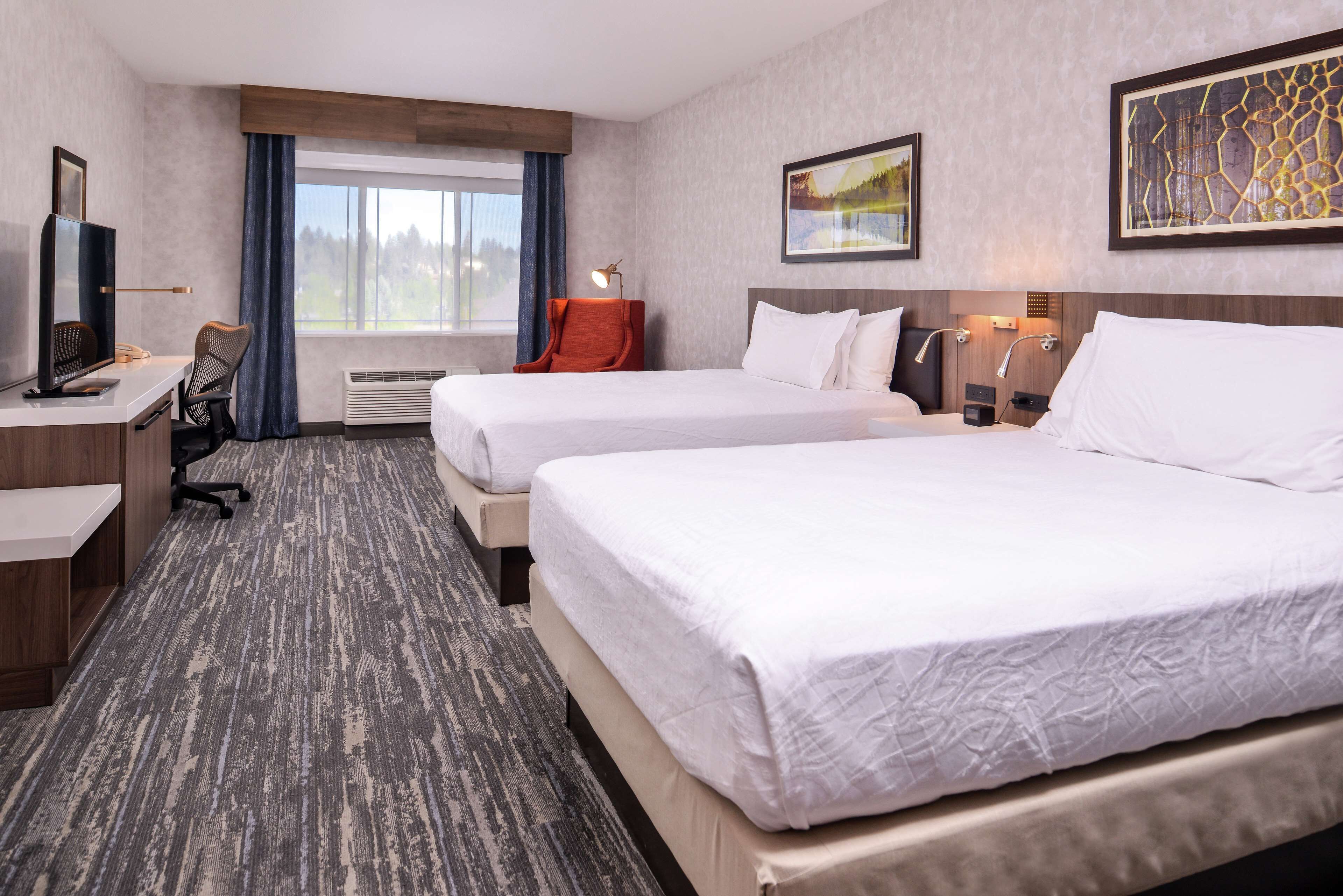 A hotel room with two beds, a desk with a computer, a chair, and a window with curtains.
