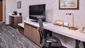 Une chambre d’hôtel équipée d’un bureau, d’un téléviseur à écran plat, d’une chaise, d’une machine à café, d’un téléphone et d’un tableau encadré au mur.
