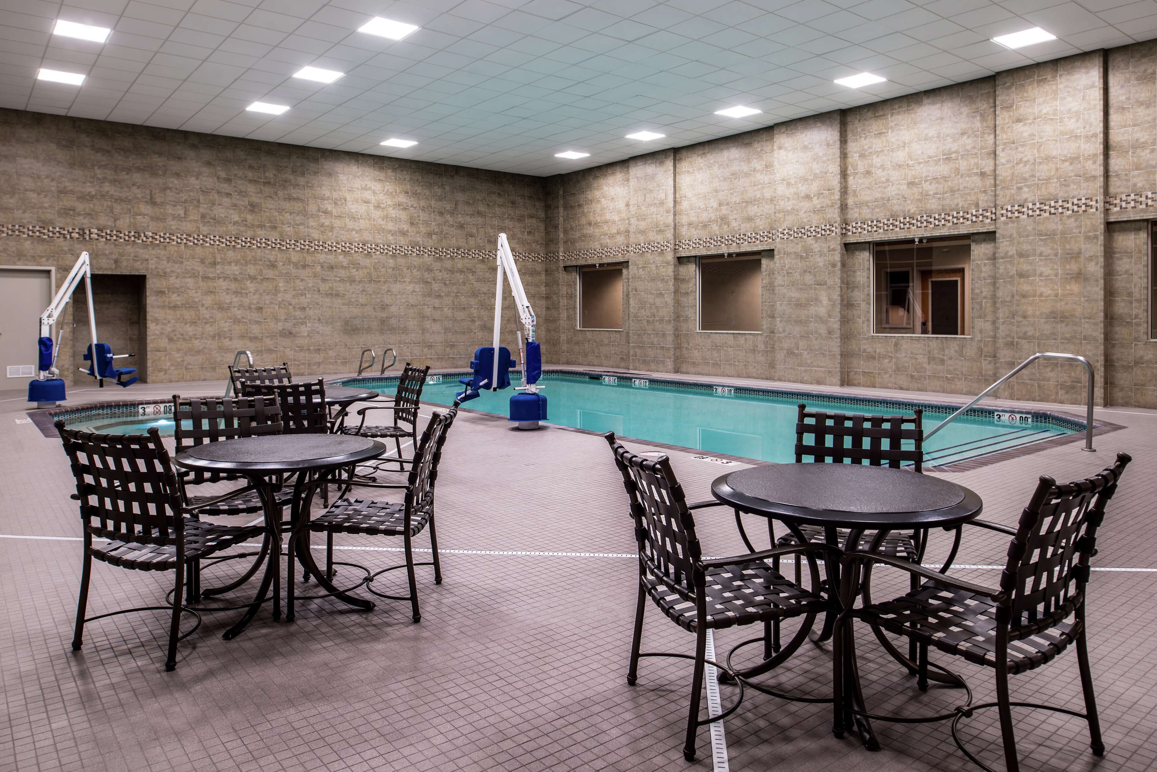 Un área de piscina con suelo de baldosas, mesas de billar y sillas.