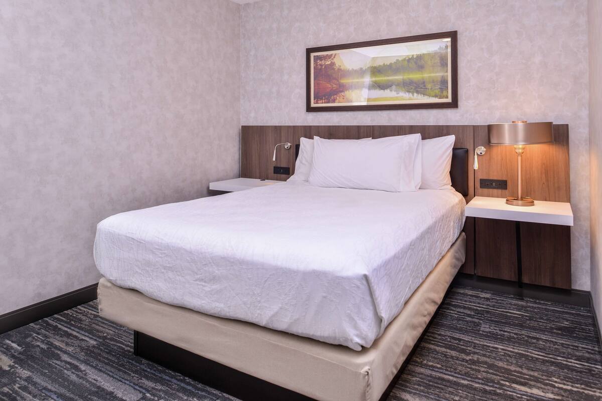 Quarto de hotel com uma cama grande, uma mesa de cabeceira, uma luminária e um quadro na parede.
