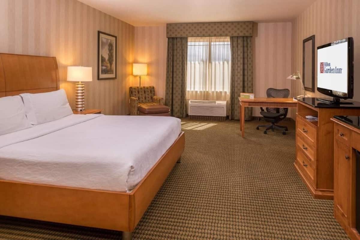 Quarto de hotel com cama, escrivaninha, televisão e uma cadeira.