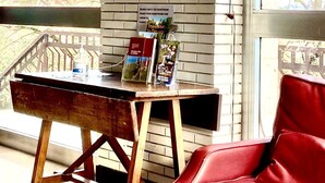 Una habitación con pared de ladrillo, un ventanal grande, un escritorio de madera, una silla roja y un espejo decorativo.