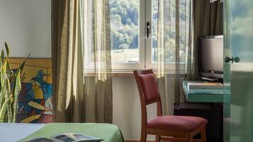 A hotel room with a bed, a chair, a desk with a television, and a window with curtains.