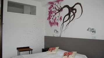 Un dormitorio con una cama grande, una mesita de noche, una pequeña mesa y una lámpara de pared.
