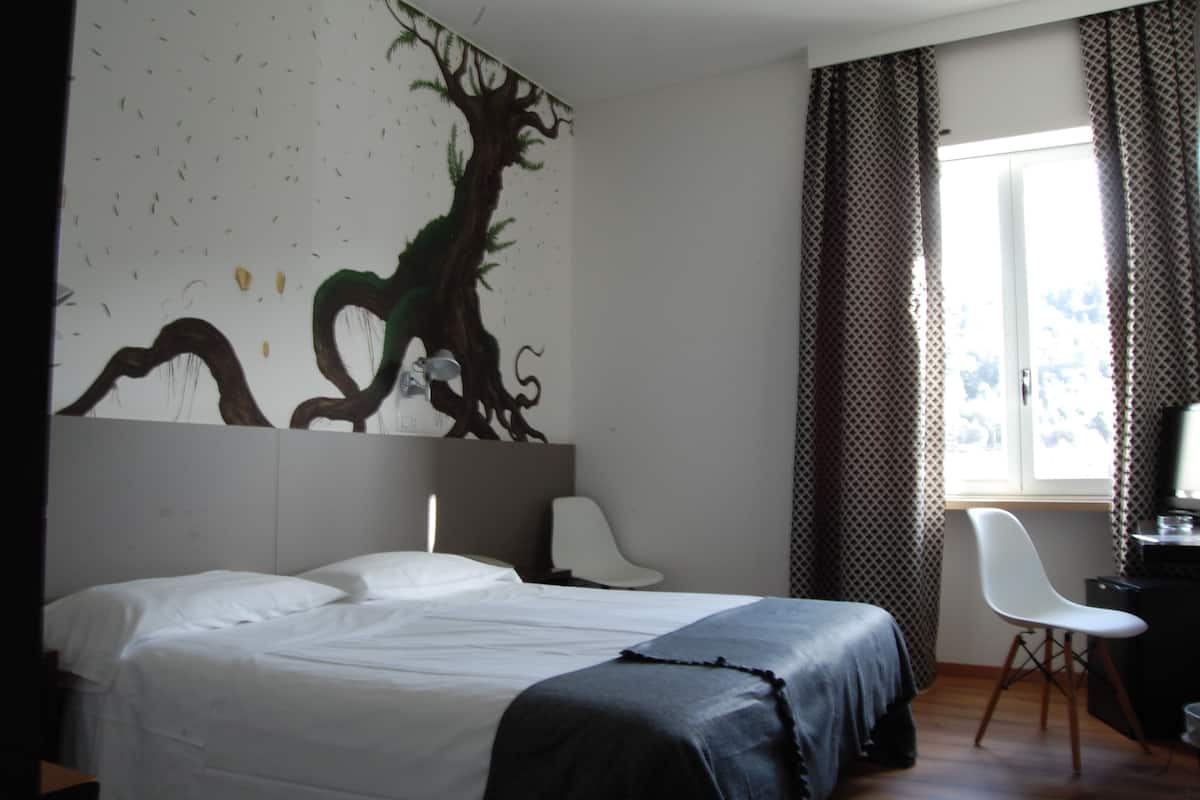 A bedroom with a bed, a chair, a desk, and a mural on the wall.