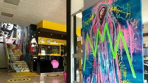 Un pasillo con un cuadro abstracto de gran tamaño, una recepción y una escalera con un mural colorido.