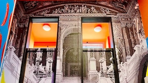 Un pasillo con un muro espejado y una escalera que lleva a una puerta con picaporte rojo.