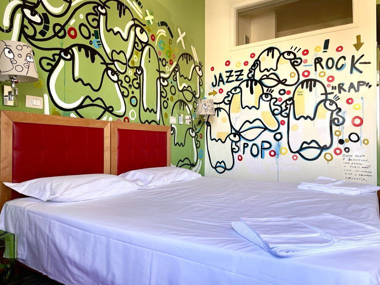 A room with a bed, a red headboard, and a wall with graffiti-style art.