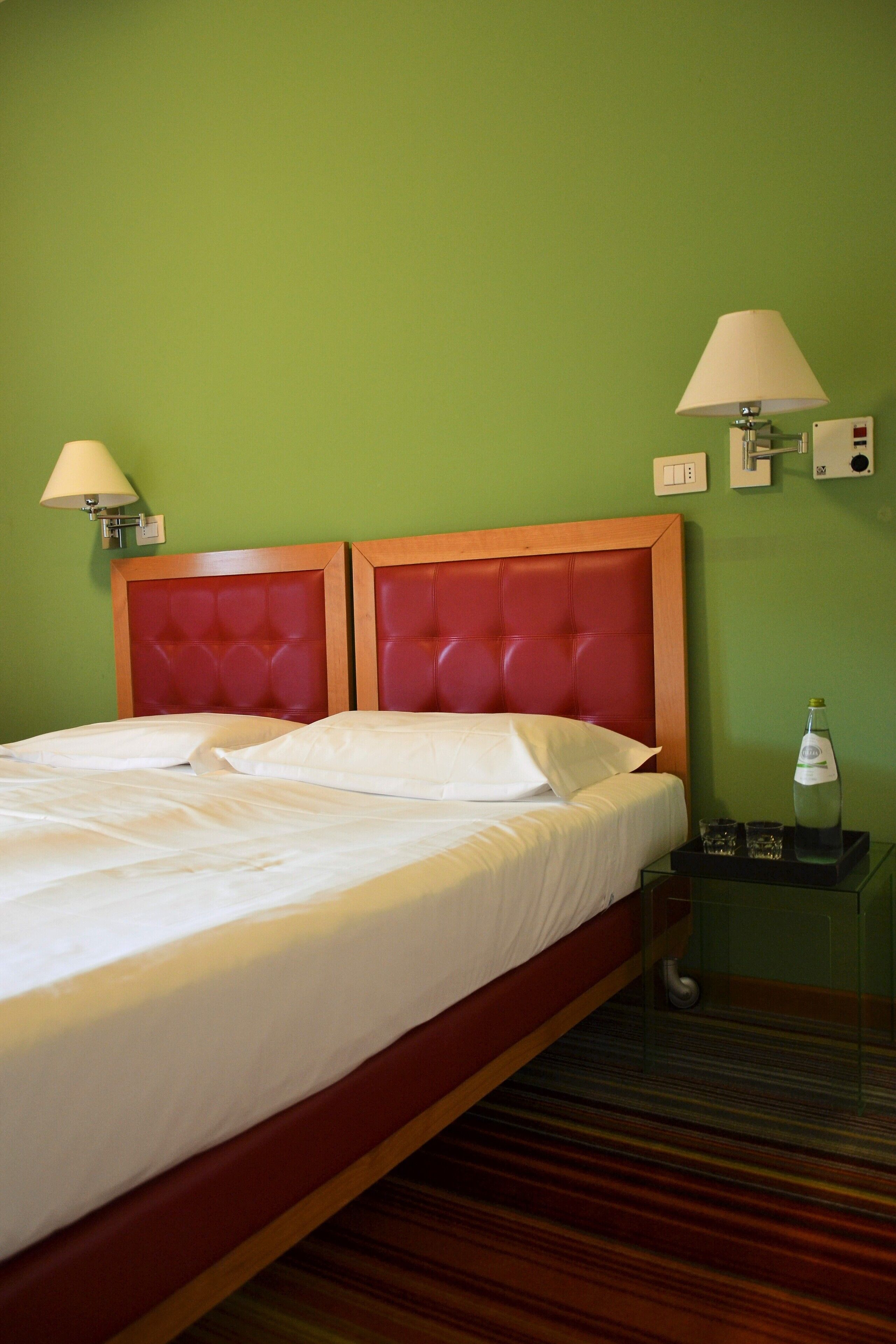 Una habitación de hotel con una cama grande, paredes verdes y una mesita de noche con una lámpara y una botella.
