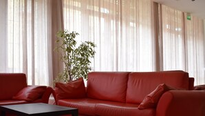 A room with a red leather sofa, a wooden coffee table, and sheer curtains. - Hotel Bamby (Rimini)
