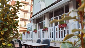 An outdoor seating area with tables and chairs, a white fence, and potted plants. - Hotel Bamby (Rimini)