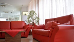 A modern living room with a red sofa set, a wooden coffee table, and a large potted plant. - Hotel Bamby (Rimini)