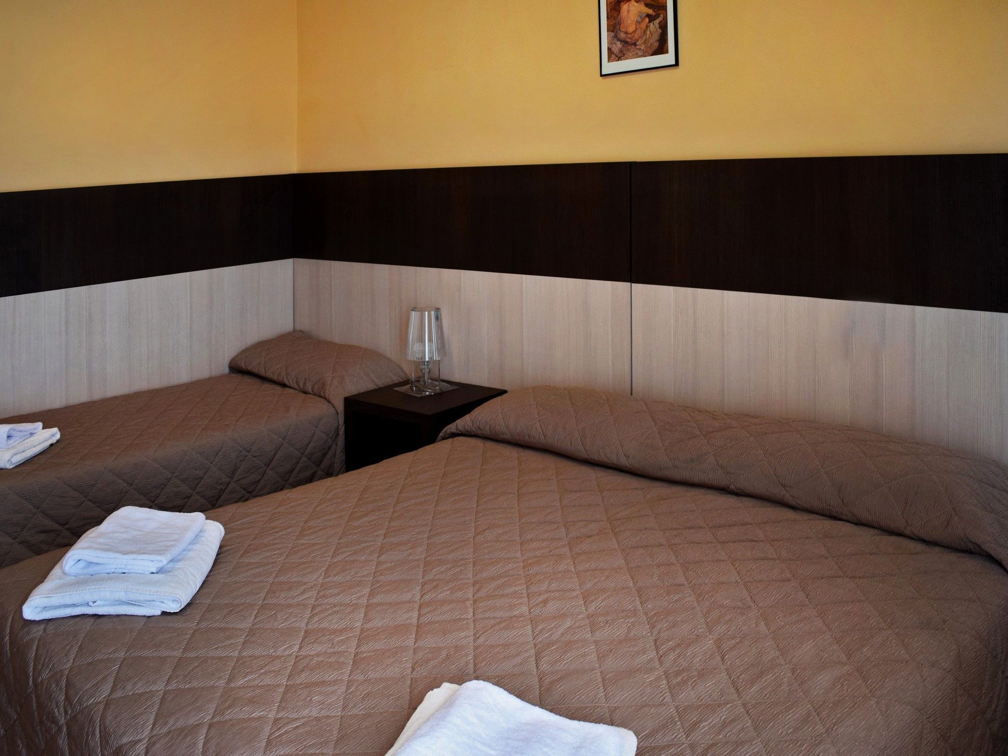 A hotel room with two beds, a nightstand, and a framed picture on the wall.