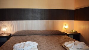 A neatly made bed with a quilted headboard, two bedside lamps, and folded towels on the bed. - Hotel Bamby (Rimini)