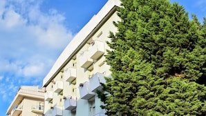 A modern building with multiple balconies, some with plants and laundry hanging. - Hotel Bamby (Rimini)