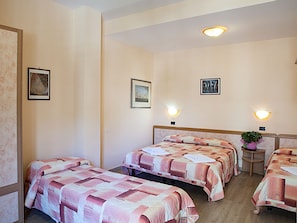 Habitación de hotel con dos camas, cabecera, luces fijadas a la pared y obras de arte enmarcadas.