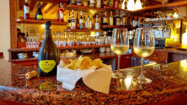 Un comptoir de bar avec une bouteille de vin, deux verres de vin blanc et un panier de chips.