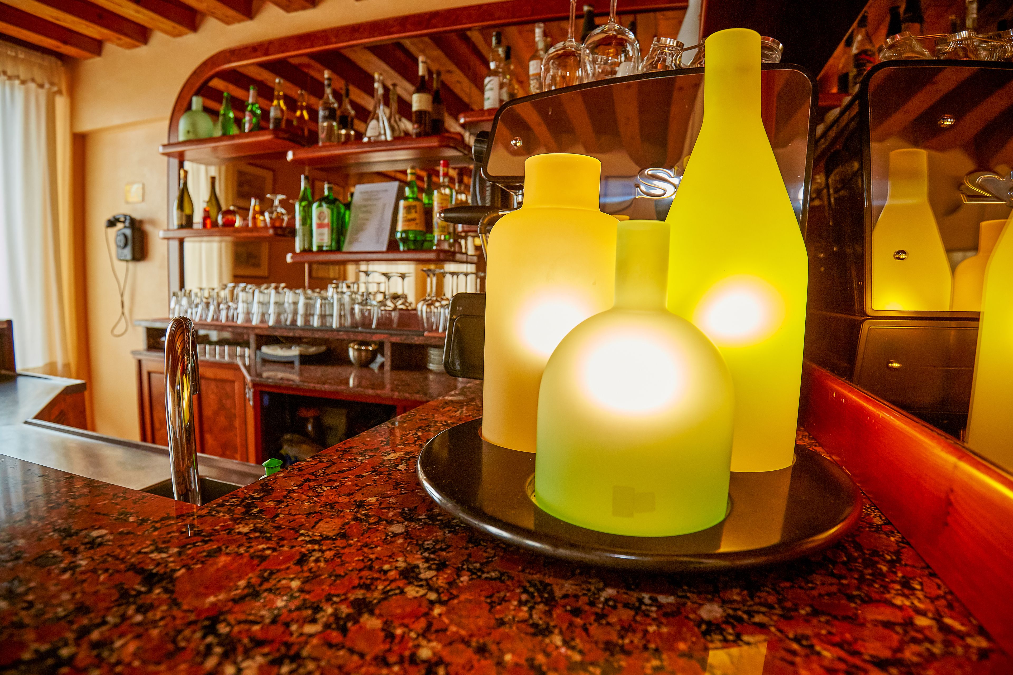 Una zona de bar con encimera de granito, un espejo y estantes con botellas y vasos.