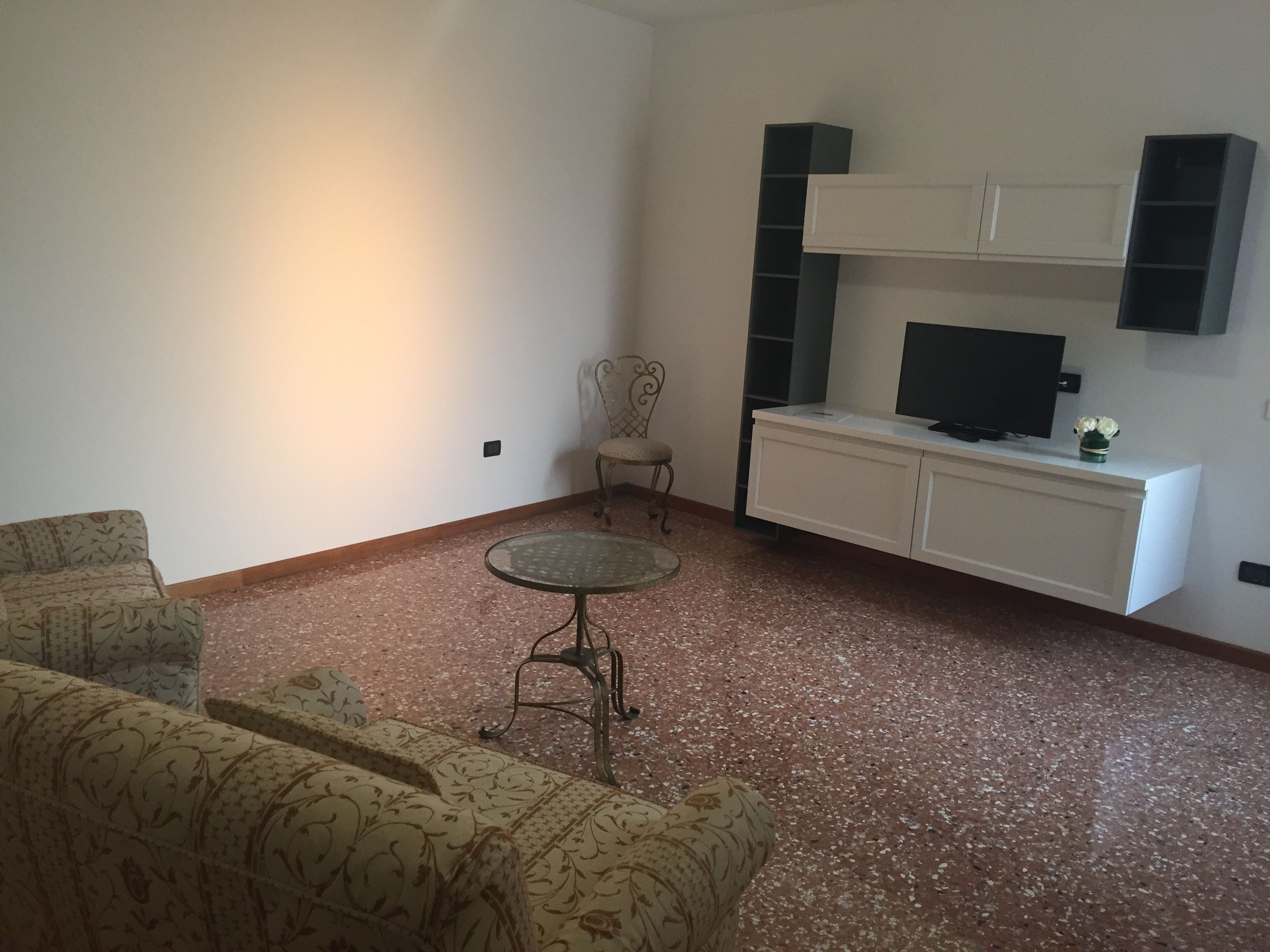 Un saló amb sofàs estampats, una taula rodona petita, un televisor sobre un moble blanc i un vas decoratiu.