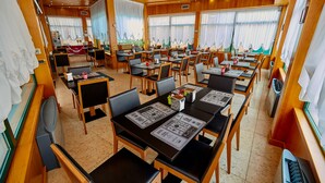 Un vaste espace dédié à la salle à manger, avec de nombreuses tables et chaises disposées en forme de U, et de grandes fenêtres qui laissent entrer la lumière naturelle.